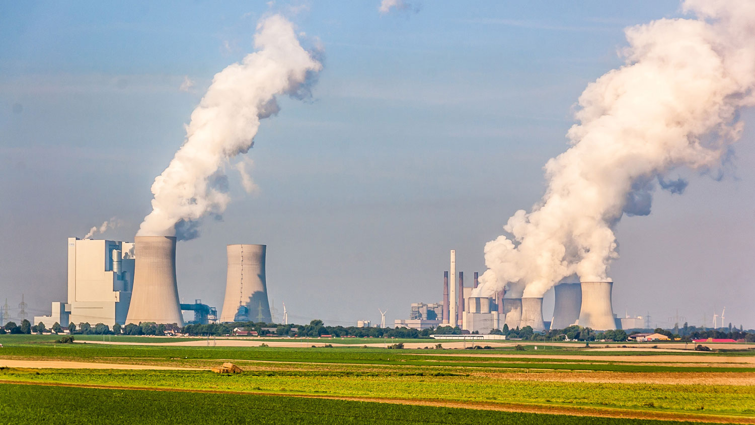 Kraftwerk mit Kühltürmen, die Dampf in den Himmel abgeben, umgeben von landwirtschaftlichen Flächen.
