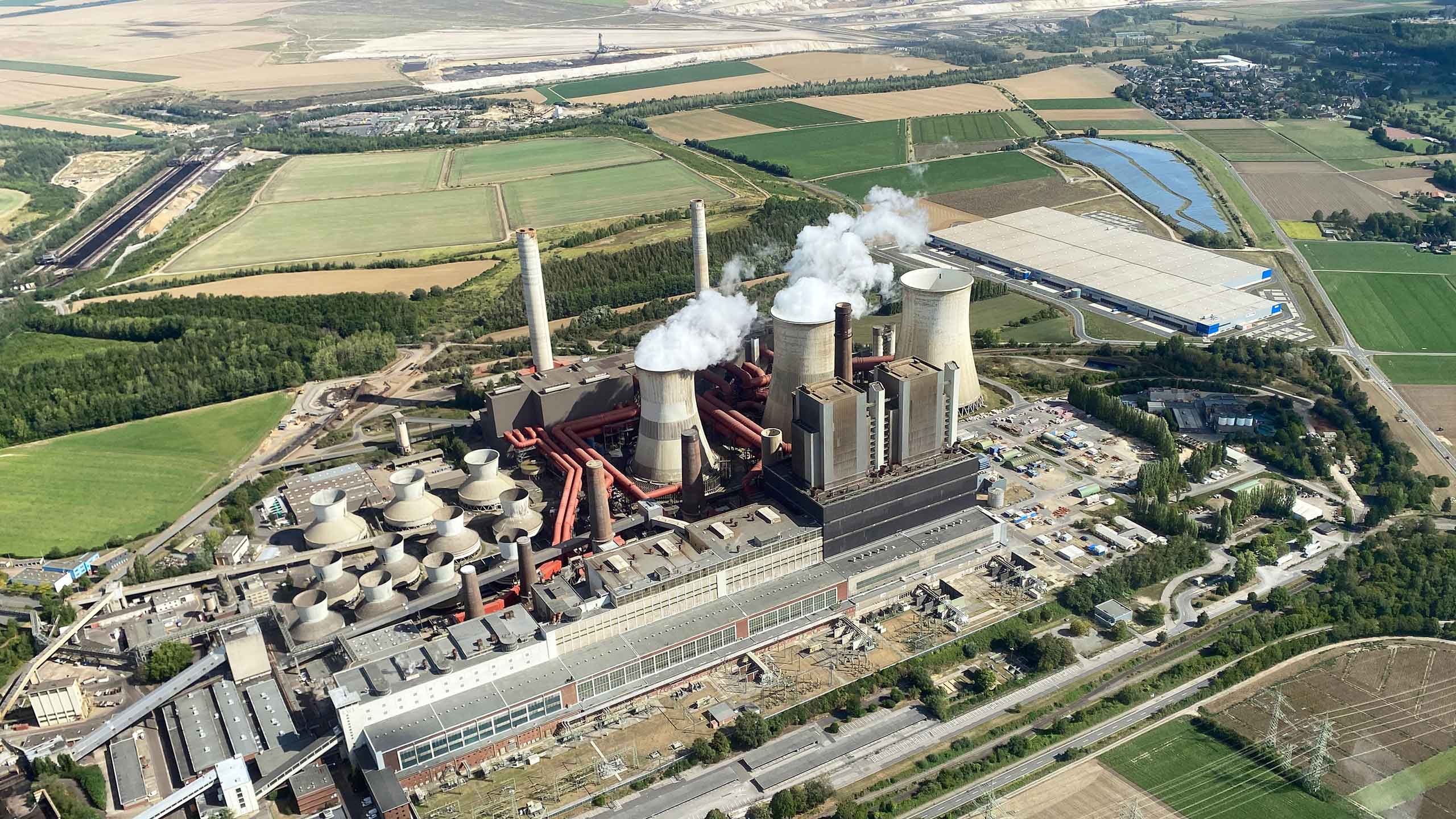 Luftaufnahme des Kraftwerks Weisweiler mit Kühltürmen, Schornsteinen und Industriegebäuden in einer ländlichen Umgebung.