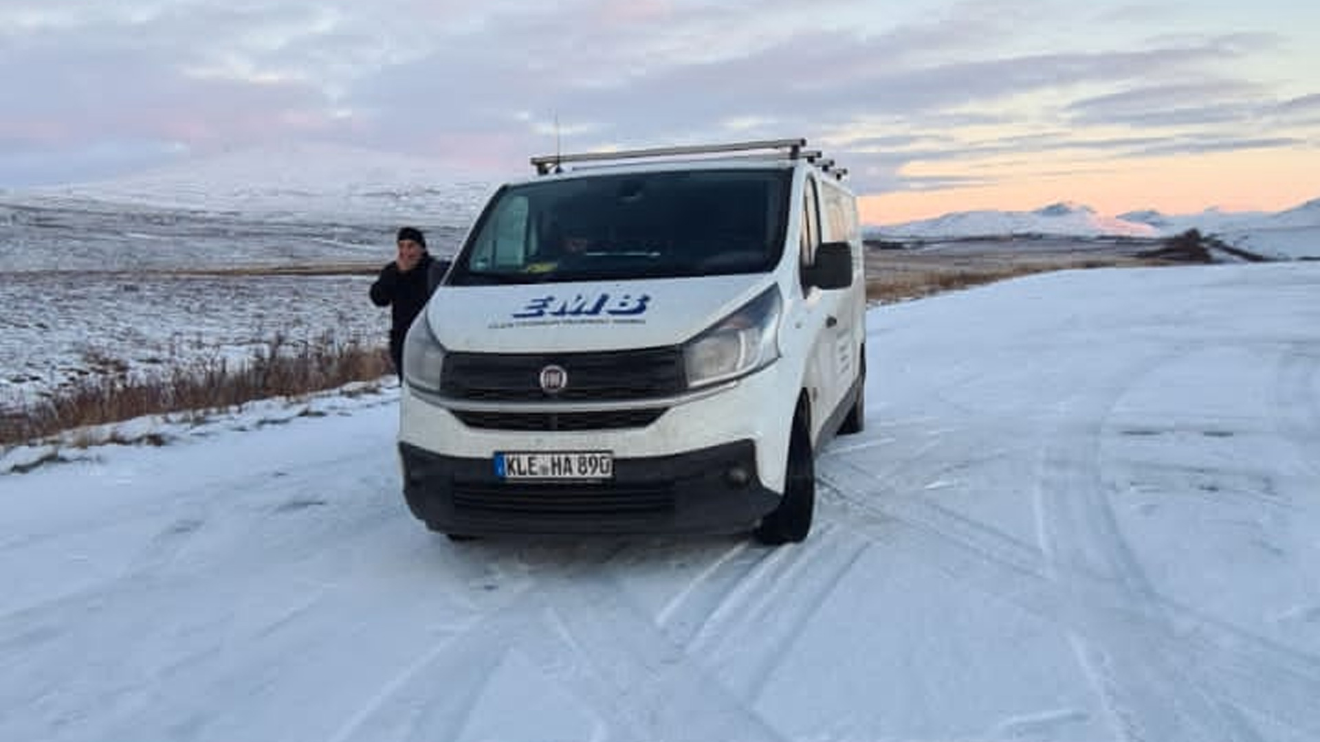 Weißes Nutzfahrzeug von EMB auf schneebedecktem Gelände mit einer Person im Hintergrund, die auf das Fahrzeug zeigt.
